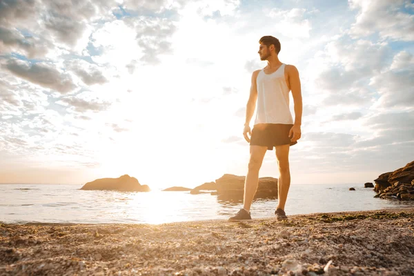 Homem atleta de pé com os braços levantados e olhando para o pôr do sol — Fotografia de Stock
