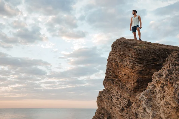 Νεαρός αθλητής που στέκεται στο βουνό βράχο δίπλα στη θάλασσα — Φωτογραφία Αρχείου