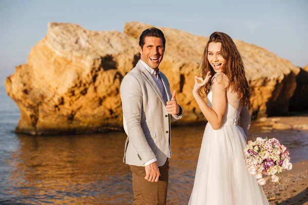 Net getrouwde paar wandelen op het strand en het tonen van ok teken — Stockfoto