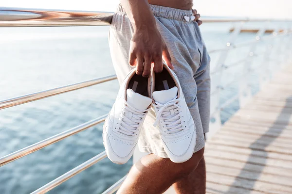 桟橋でスニーカーを保持しているスポーツマンの手の画像をトリミング — ストック写真