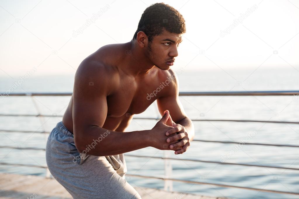 Young shirtless afro american sportsman doing squats on the pier