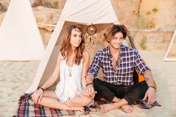 Paret sitter med benen i kors på stranden nära tält — Stockfoto