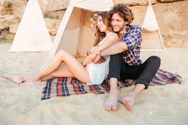 Casal abraçando e rindo perto teepee na praia — Fotografia de Stock