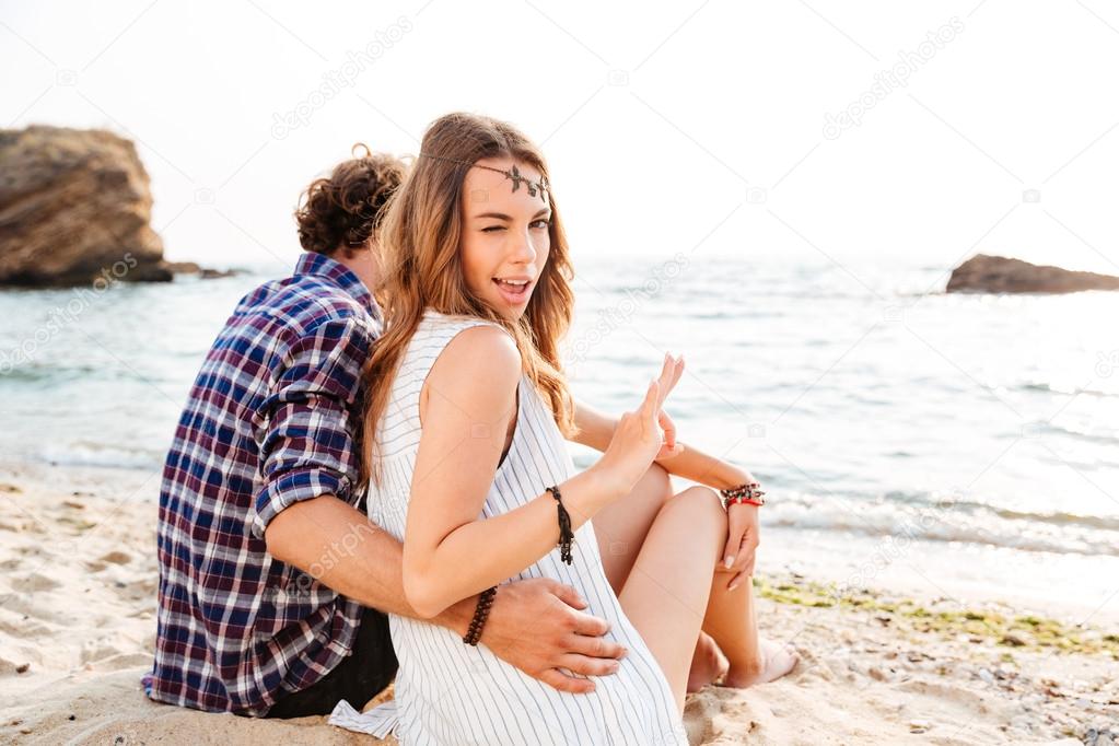 Woman sitting with boyfriend on beach and showing ok gesture