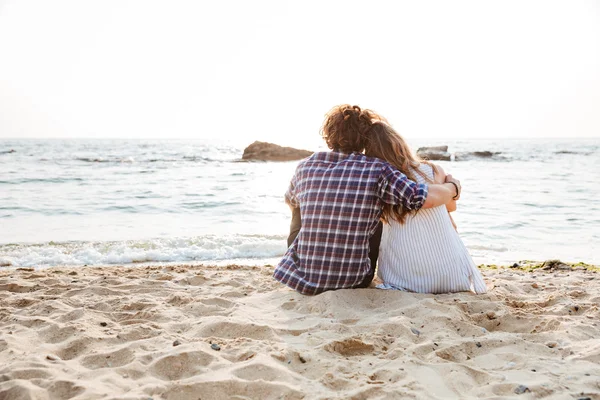 Vista trasera de pareja sentada y abrazándose en la playa — Foto de Stock