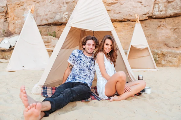 Felice giovane coppia seduta in teepee sulla spiaggia — Foto Stock