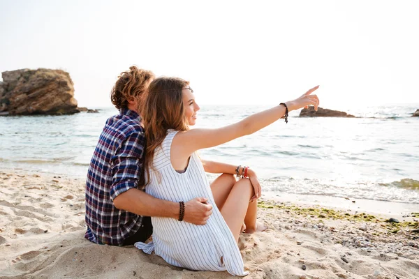 Back view of couple sitting and pointing away on beach — Stock Photo, Image