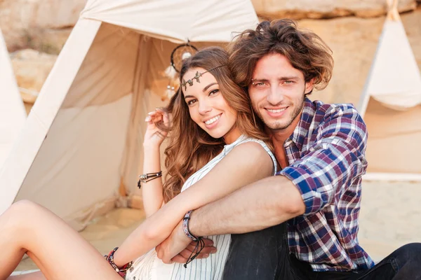 Casal sentado e abraçando perto wigwam na praia — Fotografia de Stock