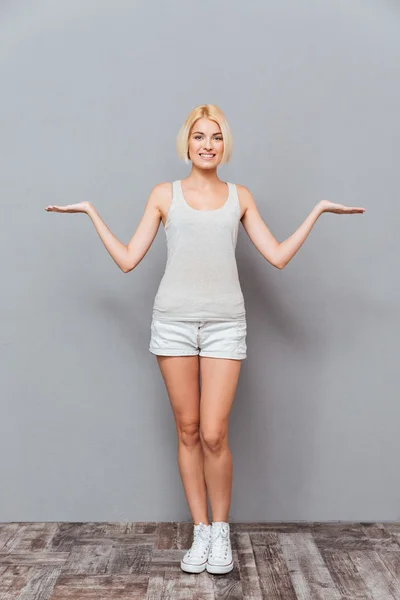 Cheerful young woman standing and holding copyspace on both palms — Stock Photo, Image