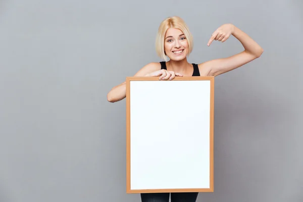 Smiling woman holding blank white board and pointing on it — Stock Photo, Image