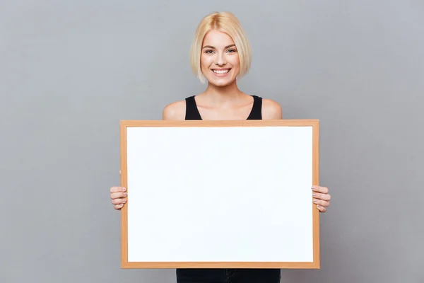 Cheerful beautiful young woman holding blank white board — Stock Photo, Image