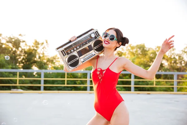 Chica en gafas de sol y traje de baño rojo sosteniendo viejo tocadiscos — Foto de Stock