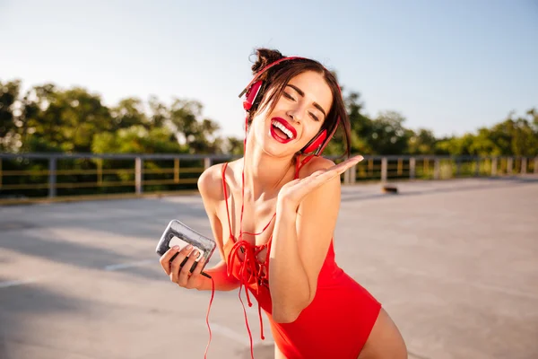 Lycklig kvinna i badkläder lyssnar på musik och sjunger utomhus — Stockfoto