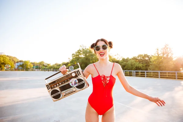 Chica en gafas de sol y traje de baño rojo sosteniendo viejo tocadiscos — Foto de Stock