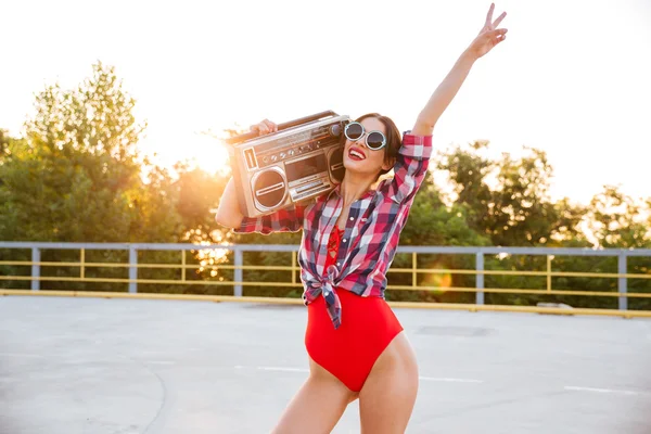 Girl in sunglasses and red swimsuit holding old record player Stock Picture