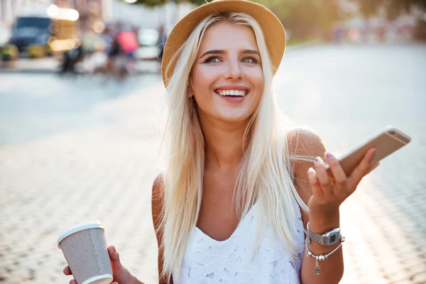 Retrato de una chica con sombrero sosteniendo la taza y el teléfono inteligente — Foto de Stock