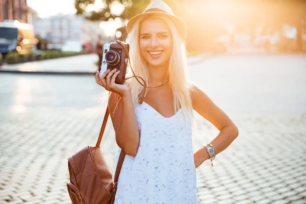 Mladá usměvavá blondýnka drží retro fotoaparát na ulici — Stock fotografie