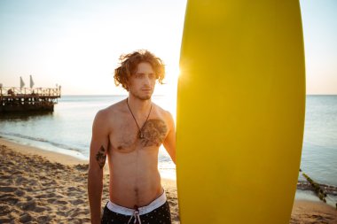 Plajda sörf tahtası dururken tutan sörfçü