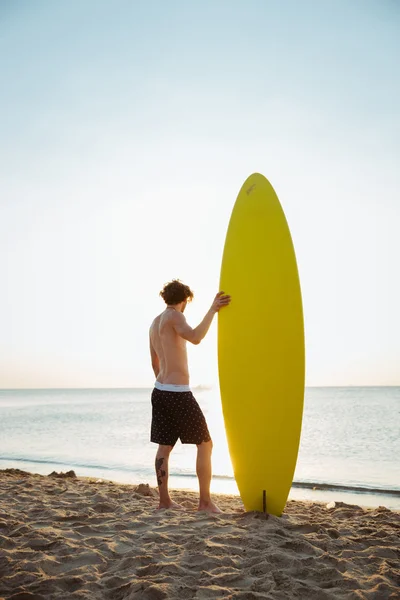 Człowiek z jego deska surfingowa stojąc na plaży — Zdjęcie stockowe
