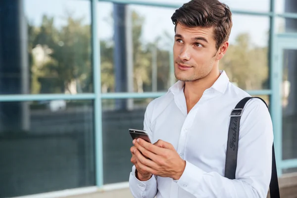 Młody przystojny biznesmen zamyślony przy użyciu telefonu komórkowego — Zdjęcie stockowe