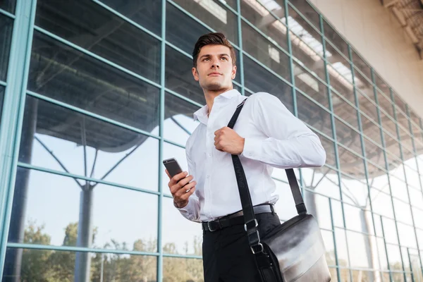 Bonito homem de negócios usando smartphone perto do prédio de escritórios — Fotografia de Stock