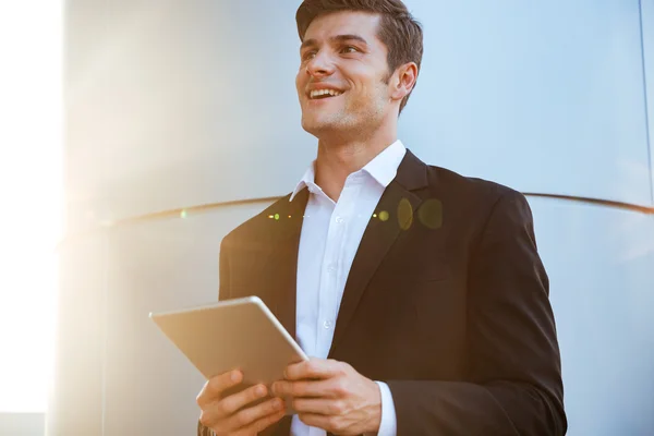 Alegre joven empresario atractivo de pie al aire libre y el uso de la tableta — Foto de Stock