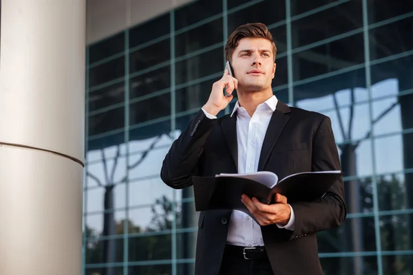 Empresario en traje sosteniendo carpetas y hablando por teléfono — Foto de Stock