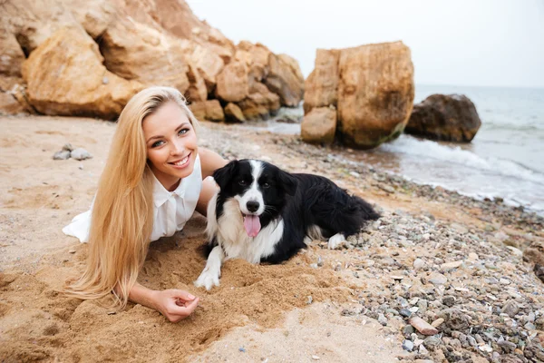 Smiling woman lying with dog on the beach — Stock Photo, Image