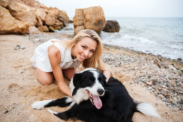 Cheerful woman hugging her dog on the beach — Stock Photo, Image