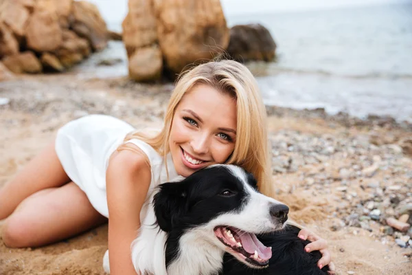Cheerful woman lying and embracing her dog on the beach — Stock Photo, Image