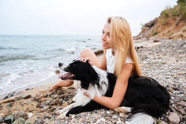 Mulher alegre sentado e descansando com o cão na praia — Fotografia de Stock