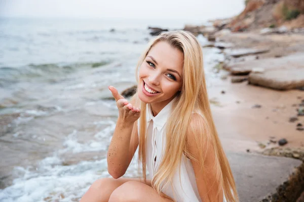 Woman blowing air kiss at rocky beach on sunny day — Stock Photo, Image