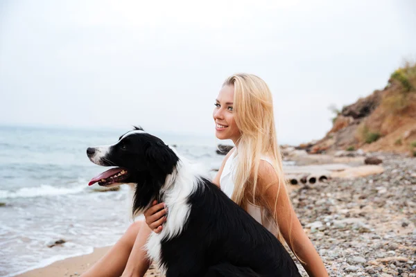 Leende kvinna med hund sitter på stranden och tänkande — Stockfoto