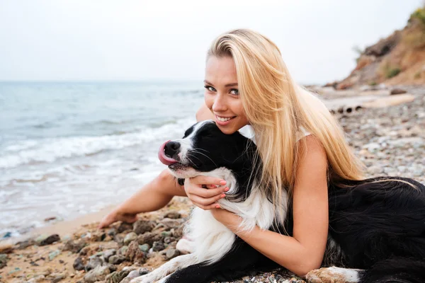 Mulher sorridente com seu cão na praia — Fotografia de Stock
