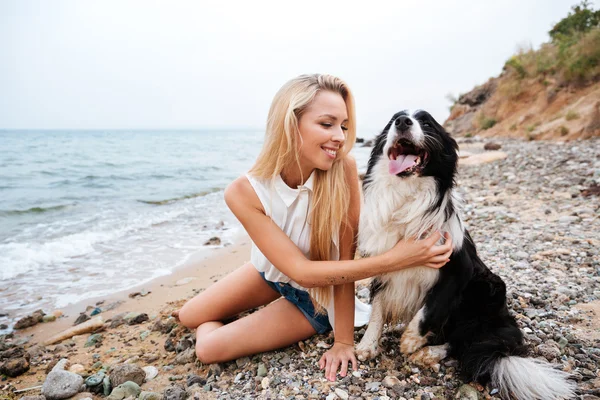 Mulher alegre sentada com seu cão na praia — Fotografia de Stock