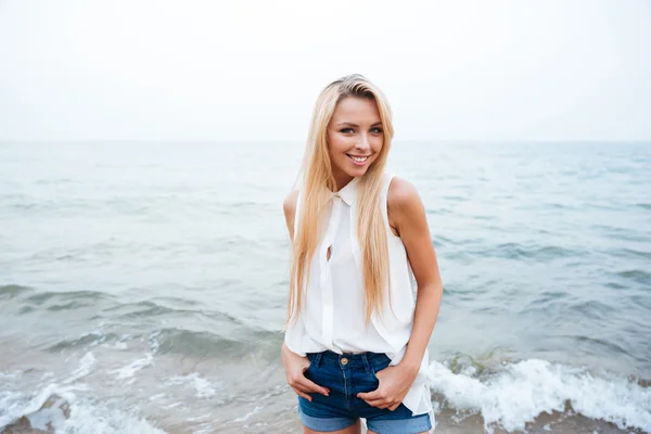 Felice giovane donna in piedi e sorridente sulla spiaggia — Foto Stock