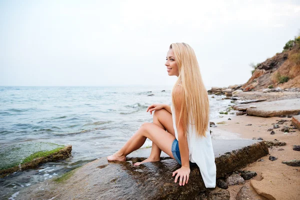 Donna sorridente con lunghi capelli biondi seduta sulla spiaggia — Foto Stock