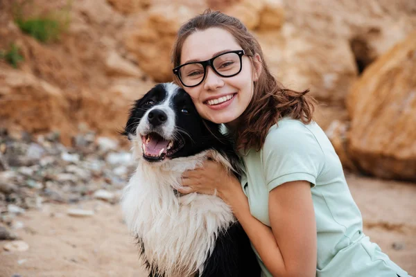 Vrolijke jonge vrouw in de hoed zitten en knuffelen haar hond — Stockfoto