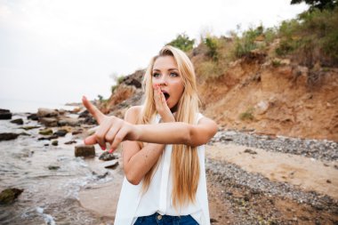 Sahilde duran ve uzağa işaret eden şaşkın kadın