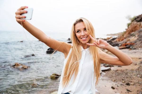 Frau zeigt V-Geste und macht Selfie am Strand — Stockfoto