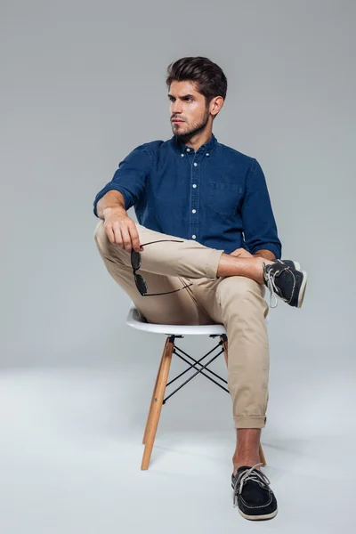 Pohledný, uvolněný muž držící brýle a sedět na židli — Stock fotografie