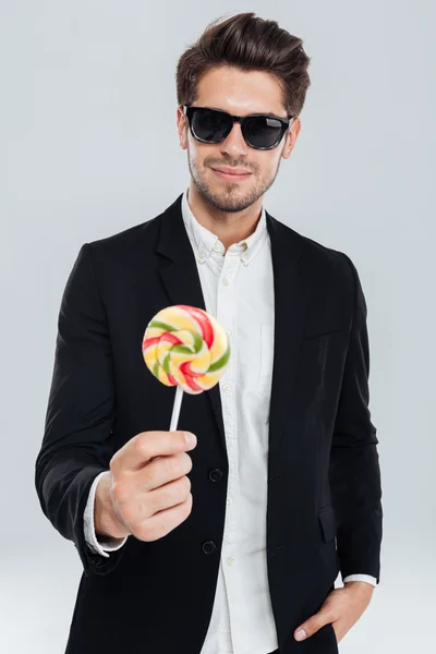 Бизнесмен в солнечных очках, стоящий с рукой в кармане, держа леденец — стоковое фото