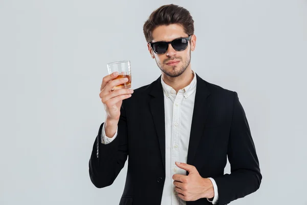 Улыбающийся счастливый бизнесмен в костюме держит стакан виски — стоковое фото