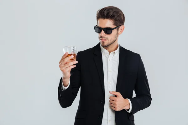 Obchodník v apartmá a sluneční brýle, pohled na whisky ve skle — Stock fotografie