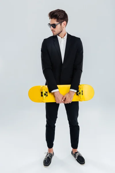 Seriös ung affärsman som innehar gul skateboard — Stockfoto
