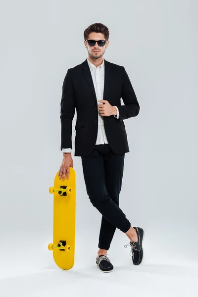 Affärsman i sunglaasses lutar på skateboard med benen korsade — Stockfoto
