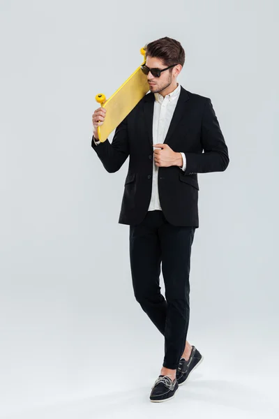 Seriöser Geschäftsmann mit Sonnenbrille und gelbem Skateboard auf dem Arm — Stockfoto