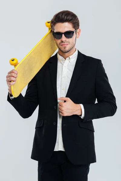 Homme d'affaires sérieux en lunettes de soleil tenant skateboard jaune sur son épaule — Photo