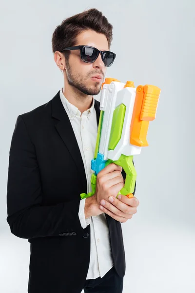 Schöner Geschäftsmann mit schwarzer Zuckerbrille und farbenfroher Wasserpistole — Stockfoto