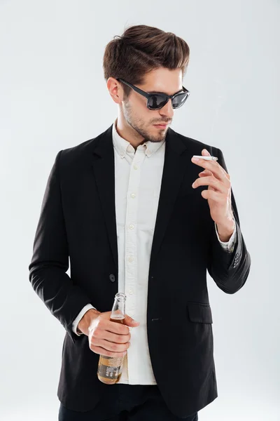 Young businessman in sunglasses holding beer bottle and smoking cigarette — Stock Photo, Image
